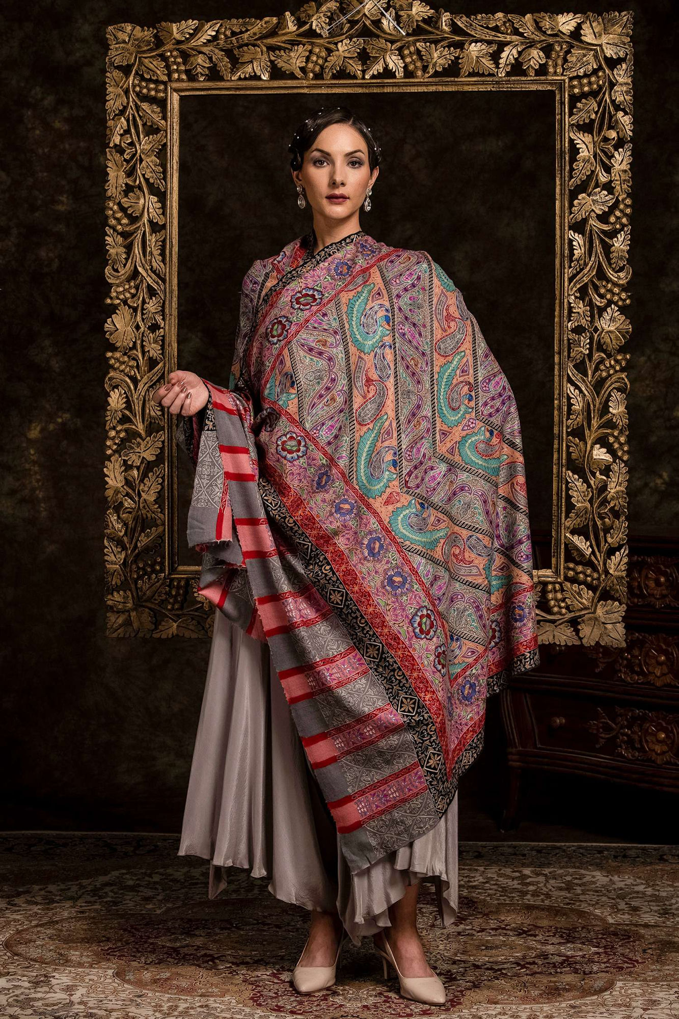 Model draped in an intricately woven paisley kani shawl in front of an ornate gilded frame